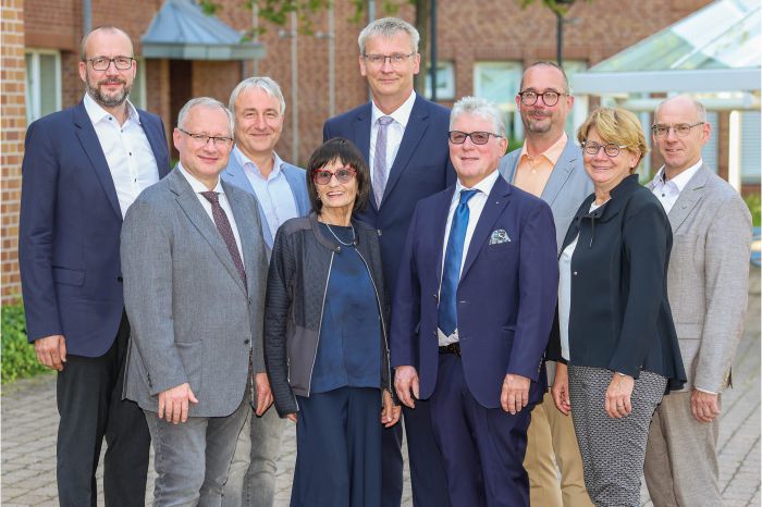 Sitzung der Ärztekammer mit zahlreichen Teilnehmern an Tischen, Vortragendem am Podium und Präsentation im Konferenzraum.