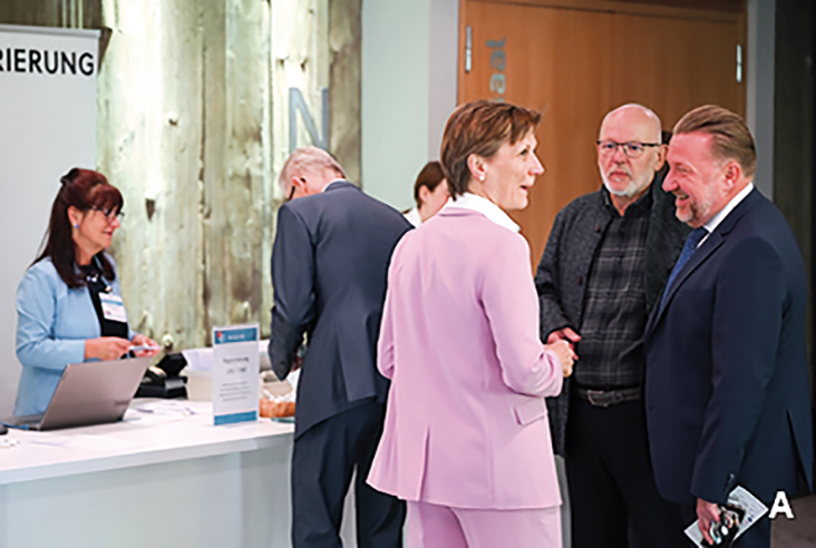 Personen im Foyer eines Kongresses im Gespräch, Registrierungstisch im Hintergrund mit Mitarbeitern.