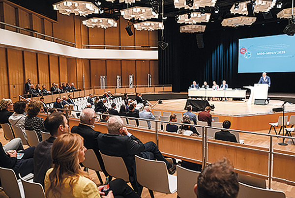Blick in einen großen Kongresssaal mit Publikum und Podium, auf dem ein medizinischer Fachvortrag gehalten wird.
