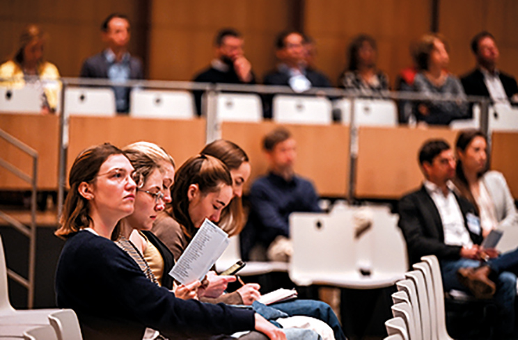 Teilnehmende sitzen im Kongresssaal, hören aufmerksam zu und machen Notizen während einer medizinischen Fachveranstaltung.